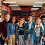 Portrait of multiracial group of high students and their teacher in a library looking at camera.