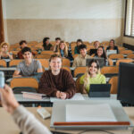 Group of multiethnic classmates smiling and listening to teacher explaining subject during lecture in classroom of modern university