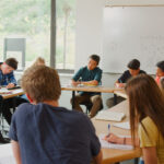 Male Tutor In Classroom Teaching High School College Or University Students In Maths Class